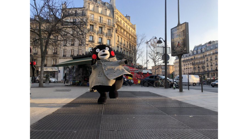 写真：フランスの街角でチェック柄コートを着てポーズを決めるくまモン